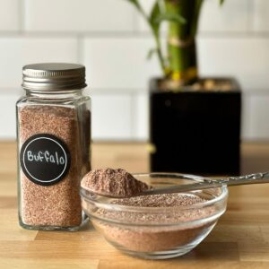 Small jar and bowl full of buffalo dry rub and a spoon full of rub with a small plant in the background.