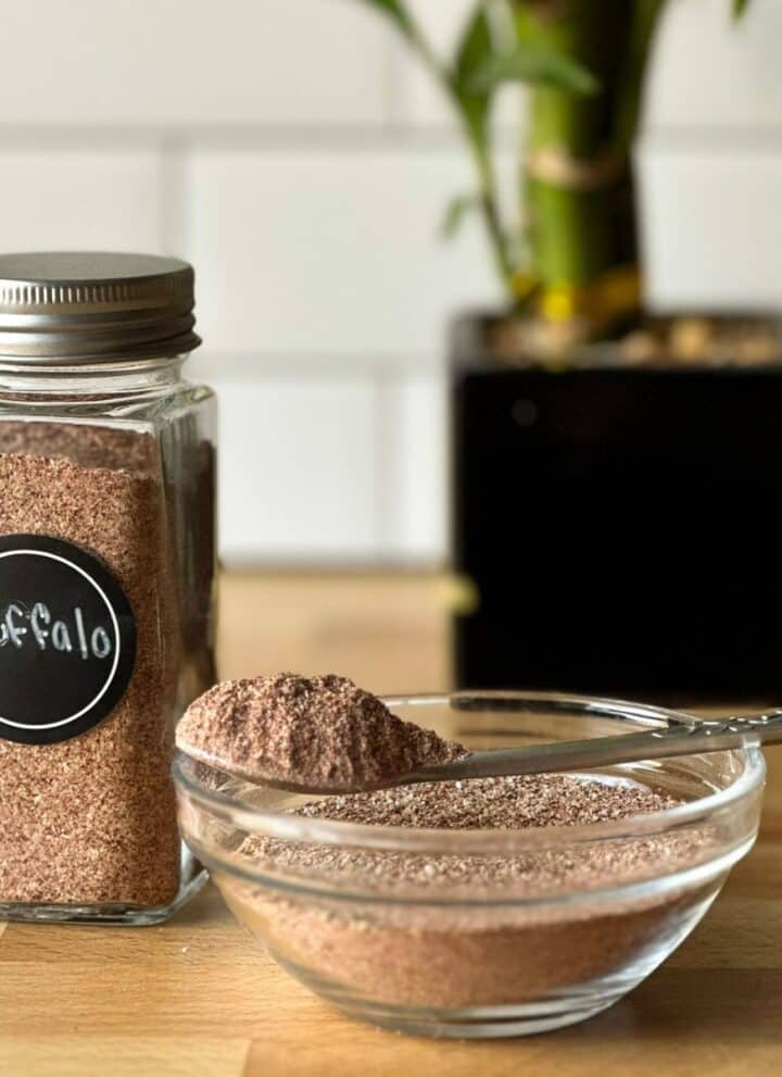 Small jar and bowl full of buffalo dry rub and a spoon full of rub with a small plant in the background.