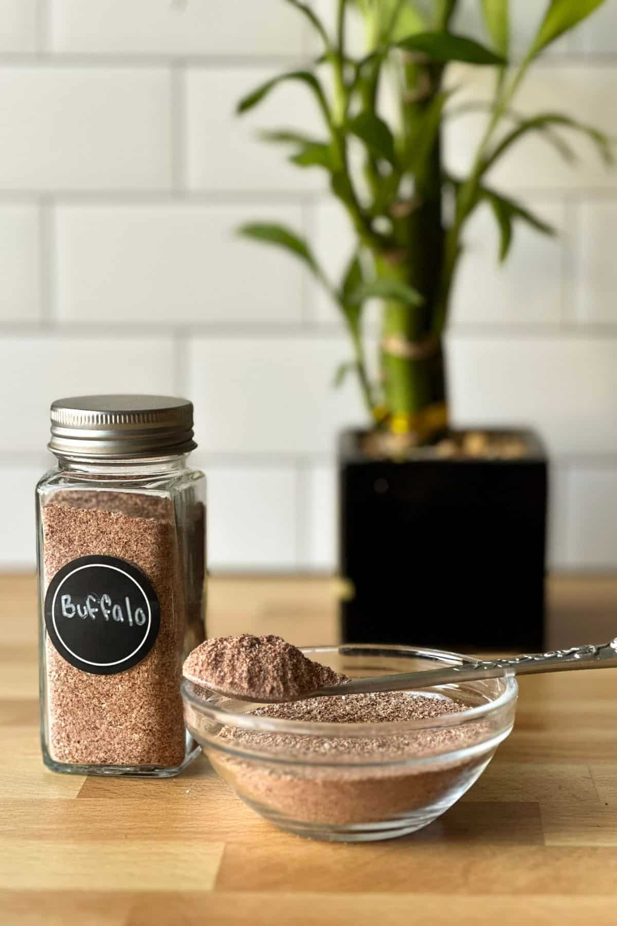 Small jar of homemade buffalo dry rub next to a small bowl and spoon full of the same rub.