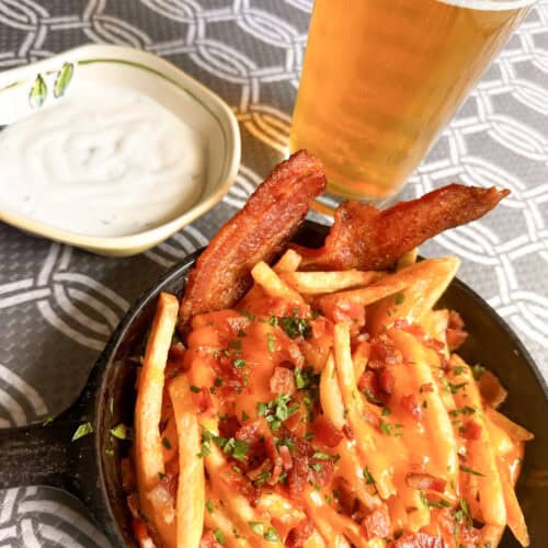 Small cast iron pan full of bacon cheese fries with a cold beer and small bowl of ranch