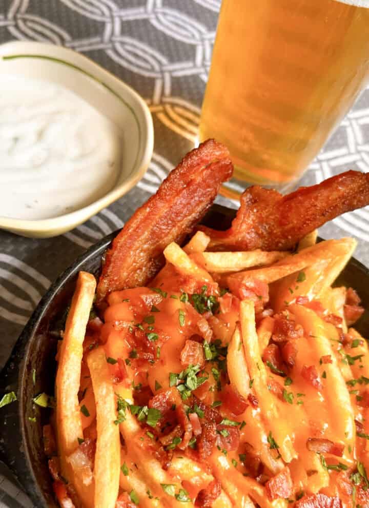 Small cast iron pan full of bacon cheese fries with a cold beer and small bowl of ranch