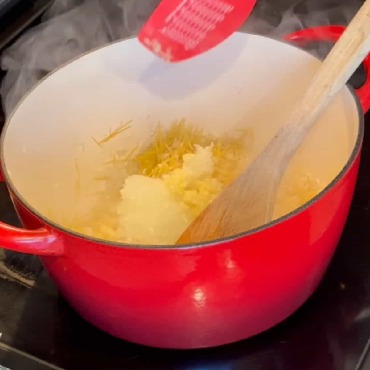 Dutch oven with onions, garlic, and salt being mixed in.