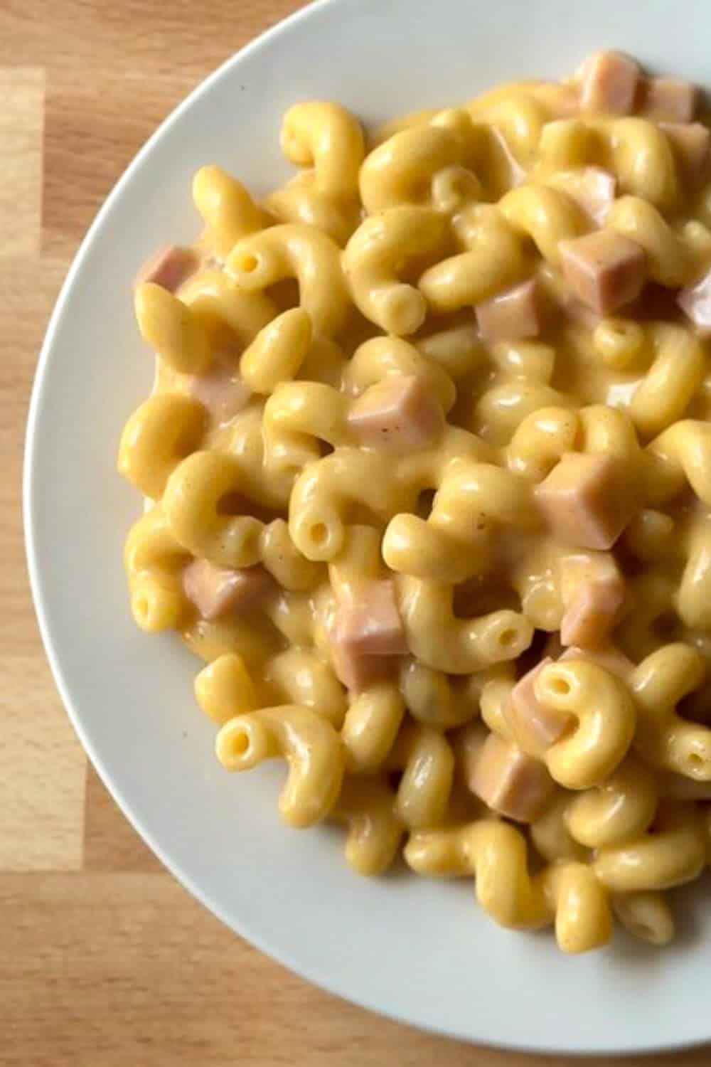 A white plate with homemade mac and cheese with cubed ham mixed in