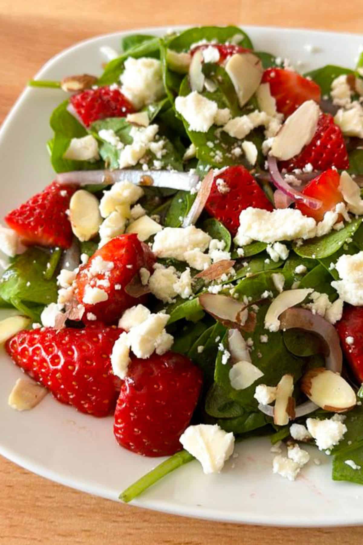 White plate with a delicious strawberry spinach salad with feta.