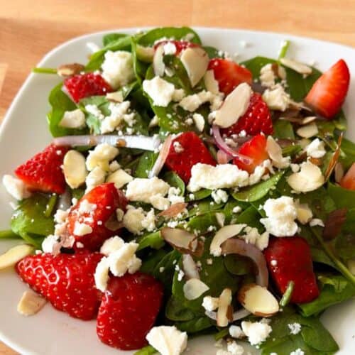 White plate with a delicious strawberry spinach salad with feta.