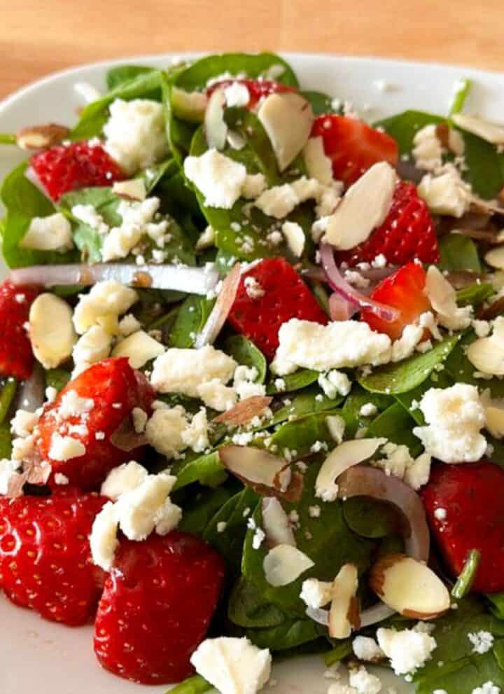 White plate with a delicious strawberry spinach salad with feta.