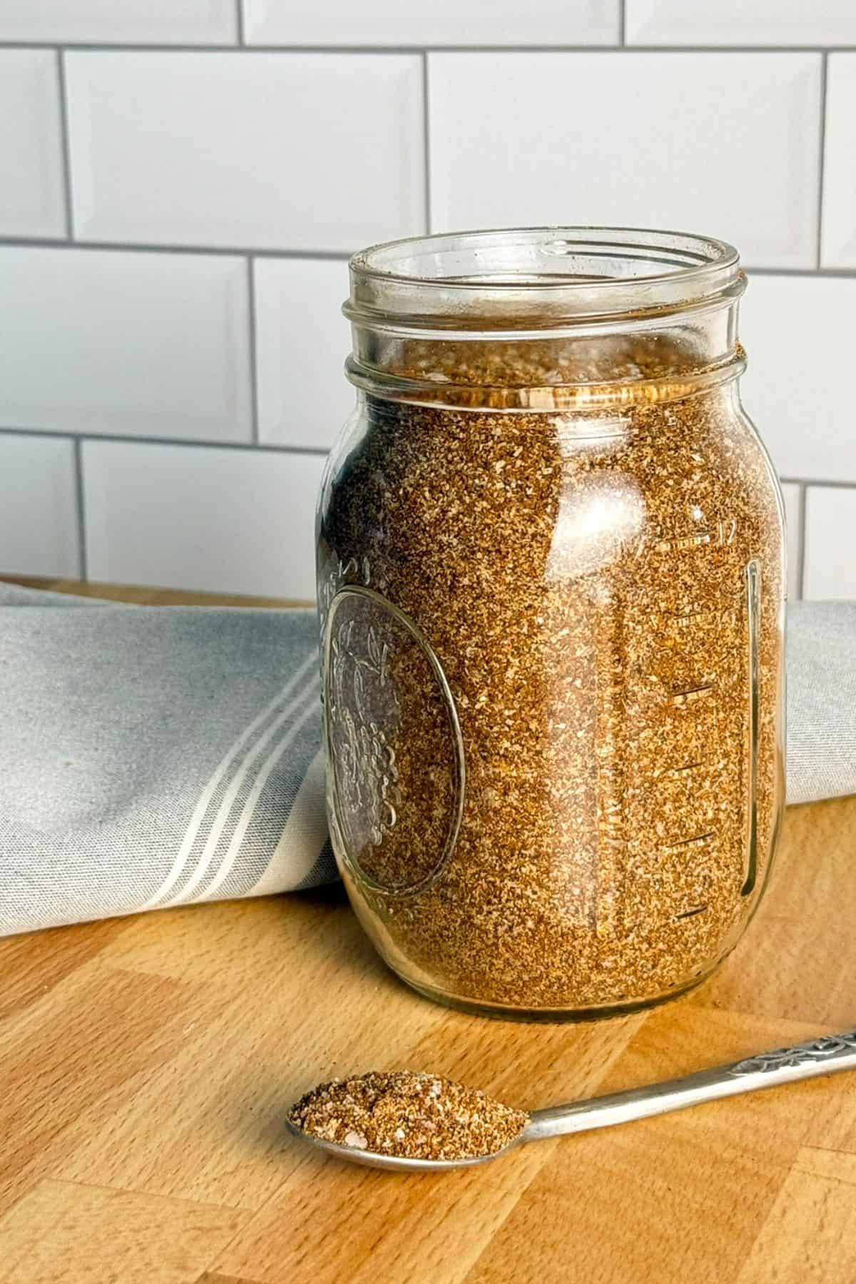Jar of sweet and smoky dry rub and a spoon of the same sitting on a butcher's block.